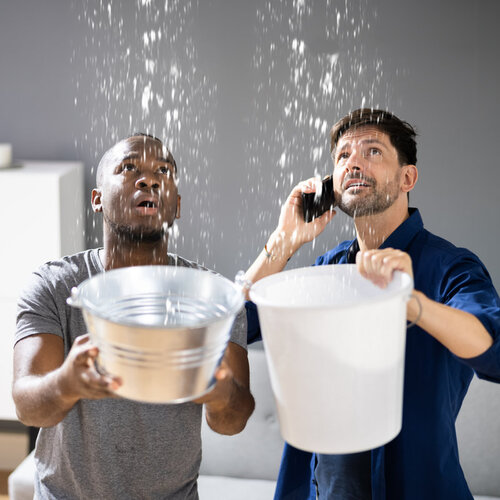 two men holding buckets under a leaking roof